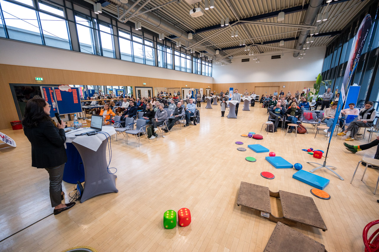 Eröffnung des Gesamtnetzwerktreffens in der Mehrzweckhalle mit interaktiven Stationen im Vordergrund.