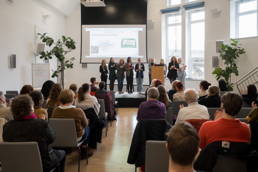 Menschen sitzen in einem veranstaltungsraum, verschiedene Personen stehen auf einer Bühne