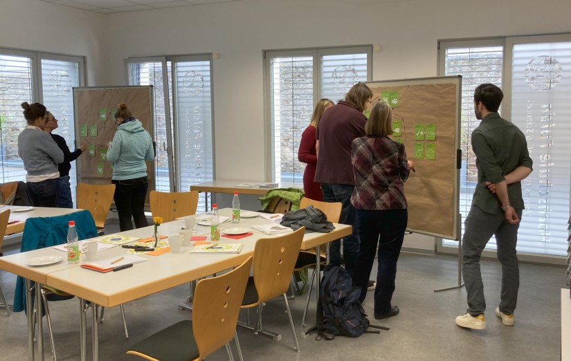 Personen stehen in einem Seminarraum vor Pinnwänden