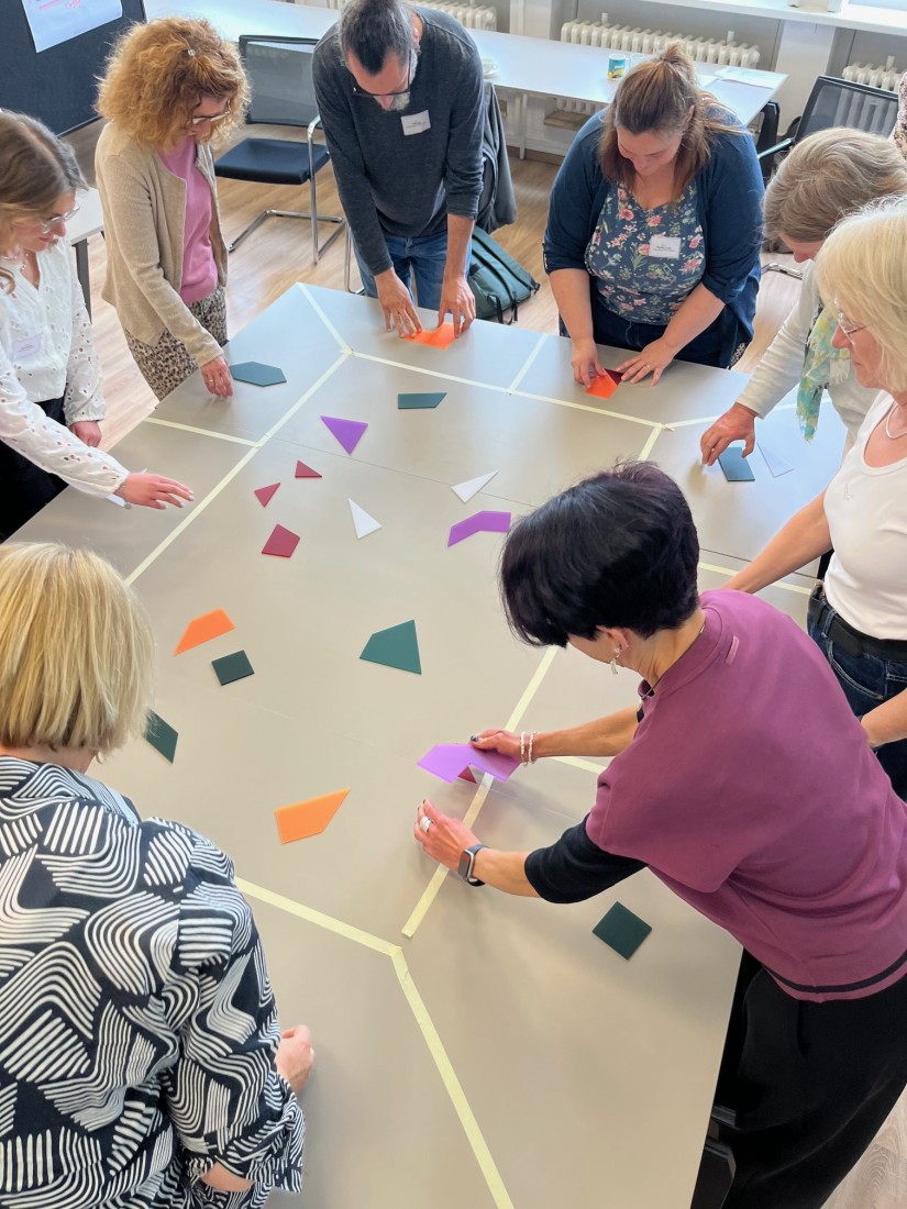 Personengruppe steht um Tisch und puzzelt mit bunten Puzzleteilen