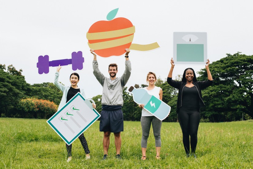 Vier Personen halten Symbole hoch, die mit dem Thema Gesundheit assoziiert sind.