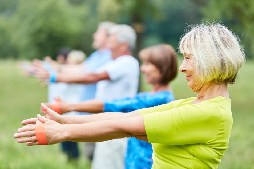 Mehrere Seniorinnen und Senioren machen eine Sportübung im Grünen