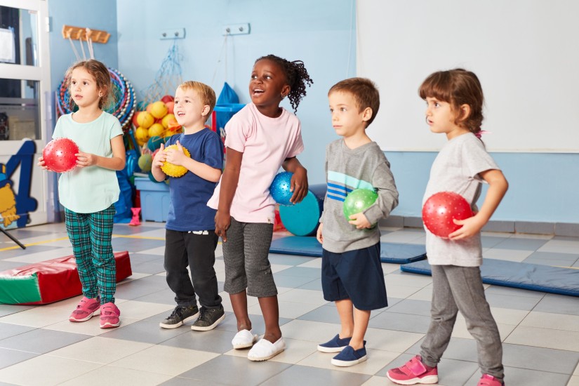 Kinder im Gymnastikraum einer Kindertagesstätte mit bunten Bällen in der Hand
